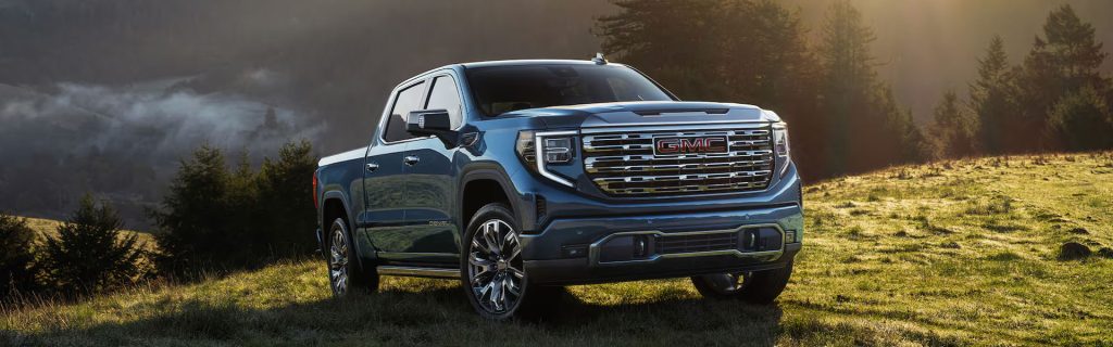 Blue GMC 2026 Sierra pickup truck parked on grassy terrain with hills in the background