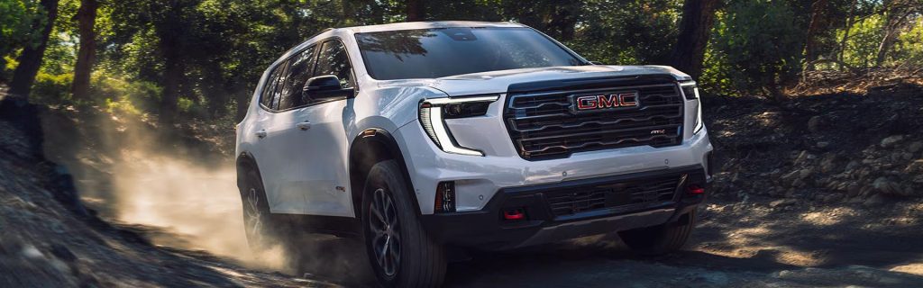 White GMC SUV driving through a forest trail.
