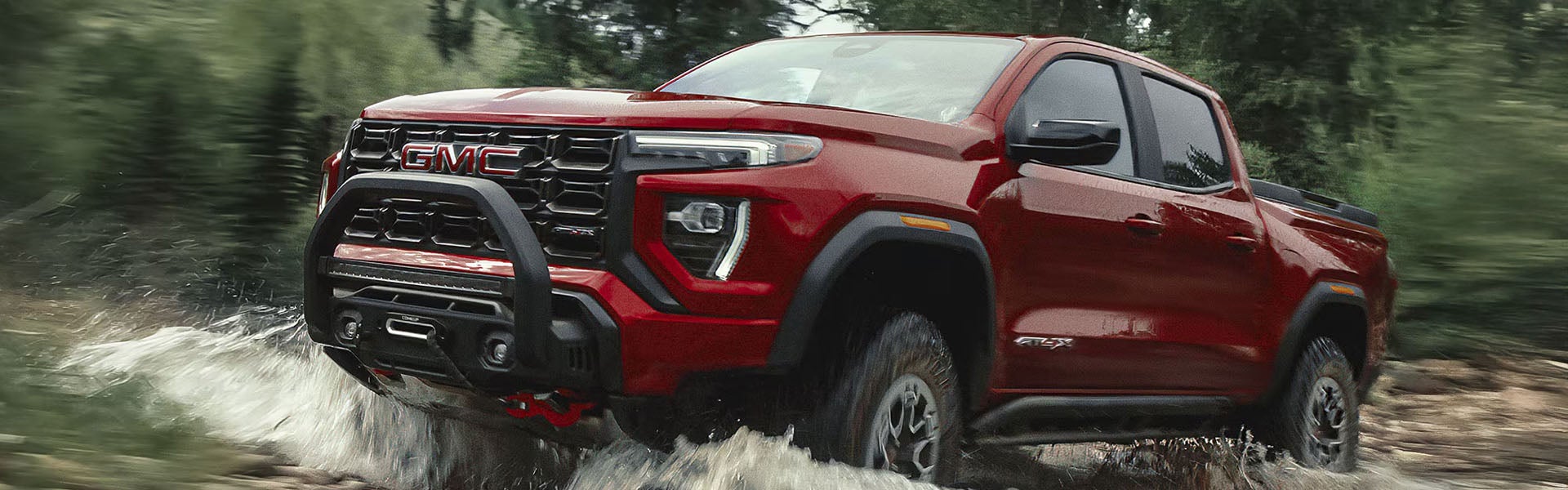 Red GMC pickup truck driving through shallow water on an off-road trail.